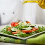 Food concept. Chef is pouring olive oil over fresh salad in restaurant kitchen.